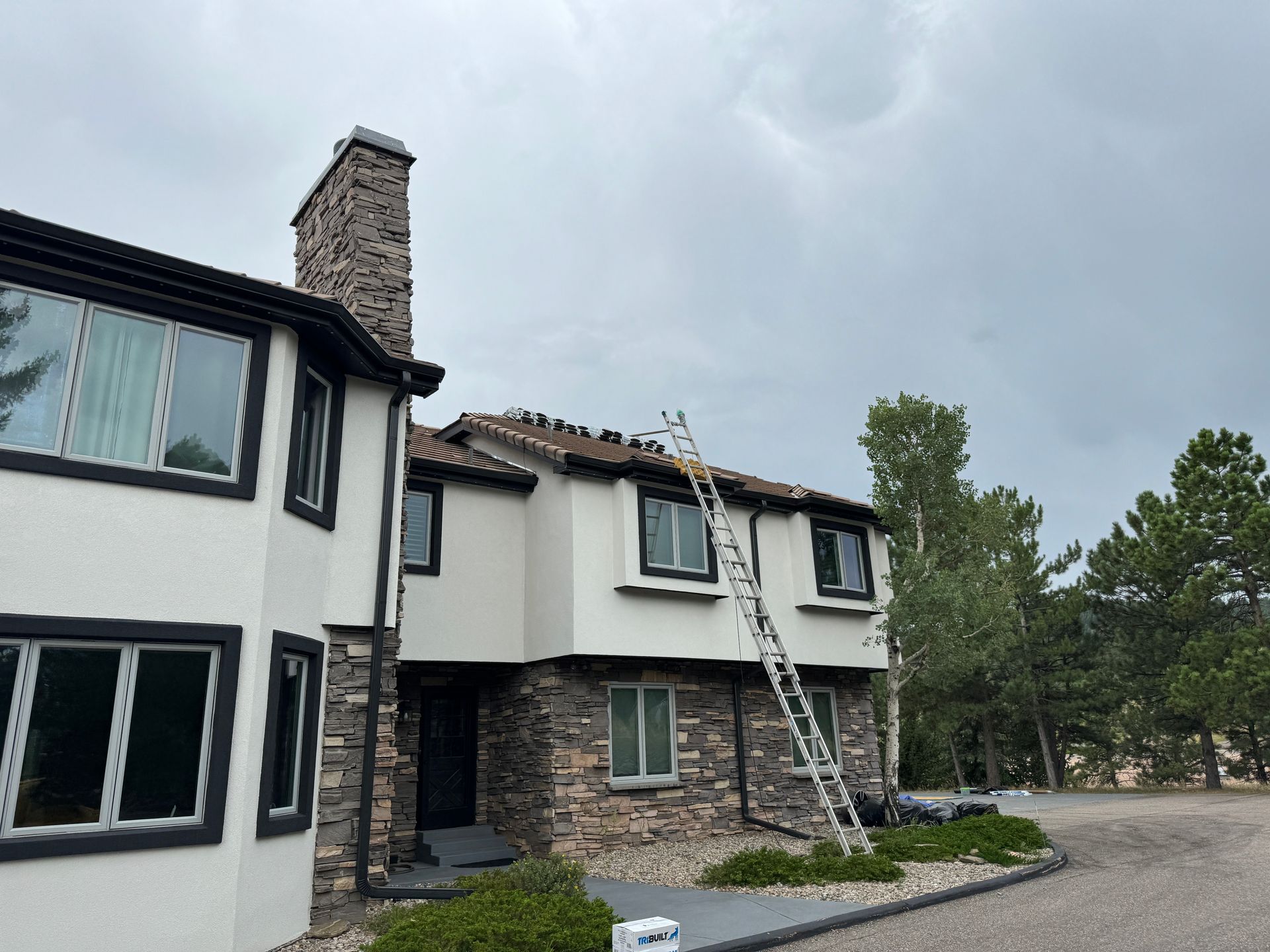 Two-story house with a ladder on the roof under an overcast sky.