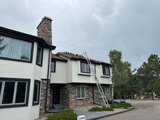 Two-story house with a ladder on the roof under an overcast sky.
