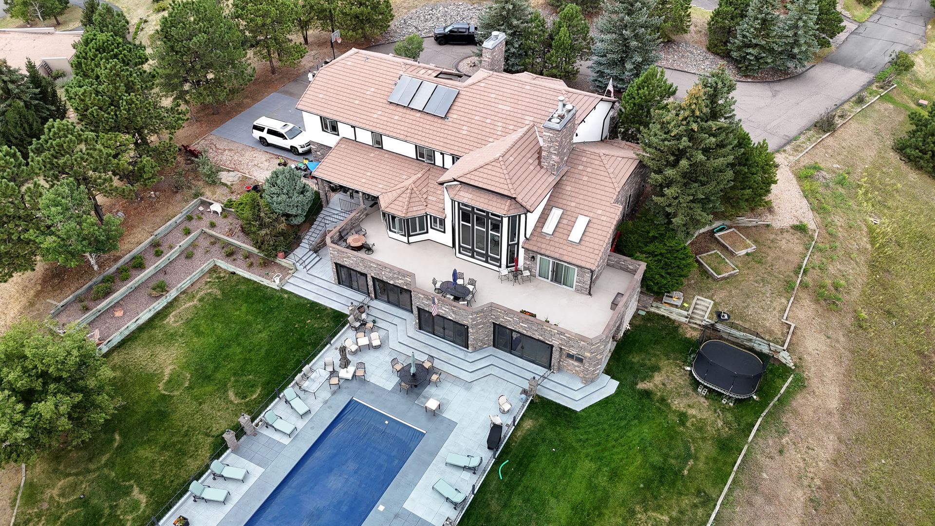 Aerial view of a large, stone-faced house with a pool, surrounded by trees and grass.