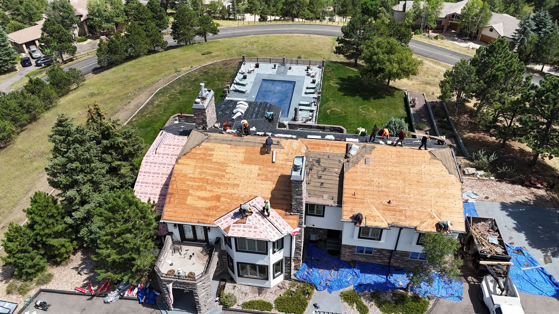 Aerial view of a house with roof replacement in progress; a pool, and neighborhood in the background.