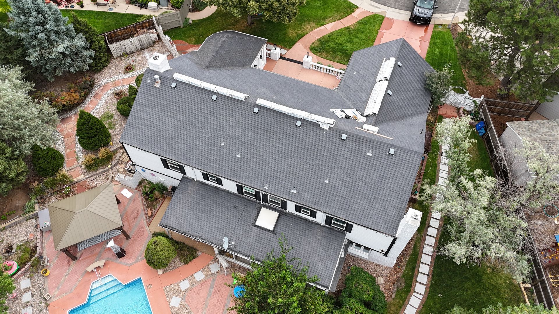 Aerial view of a white house with a dark gray roof, a pool, and surrounding landscaping.