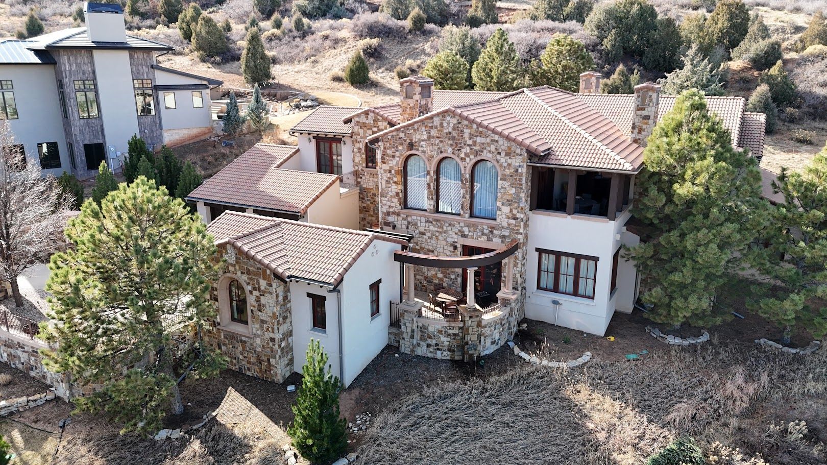 Aerial view of a luxury home with a pool, surrounded by trees, and vehicles parked in the driveway.