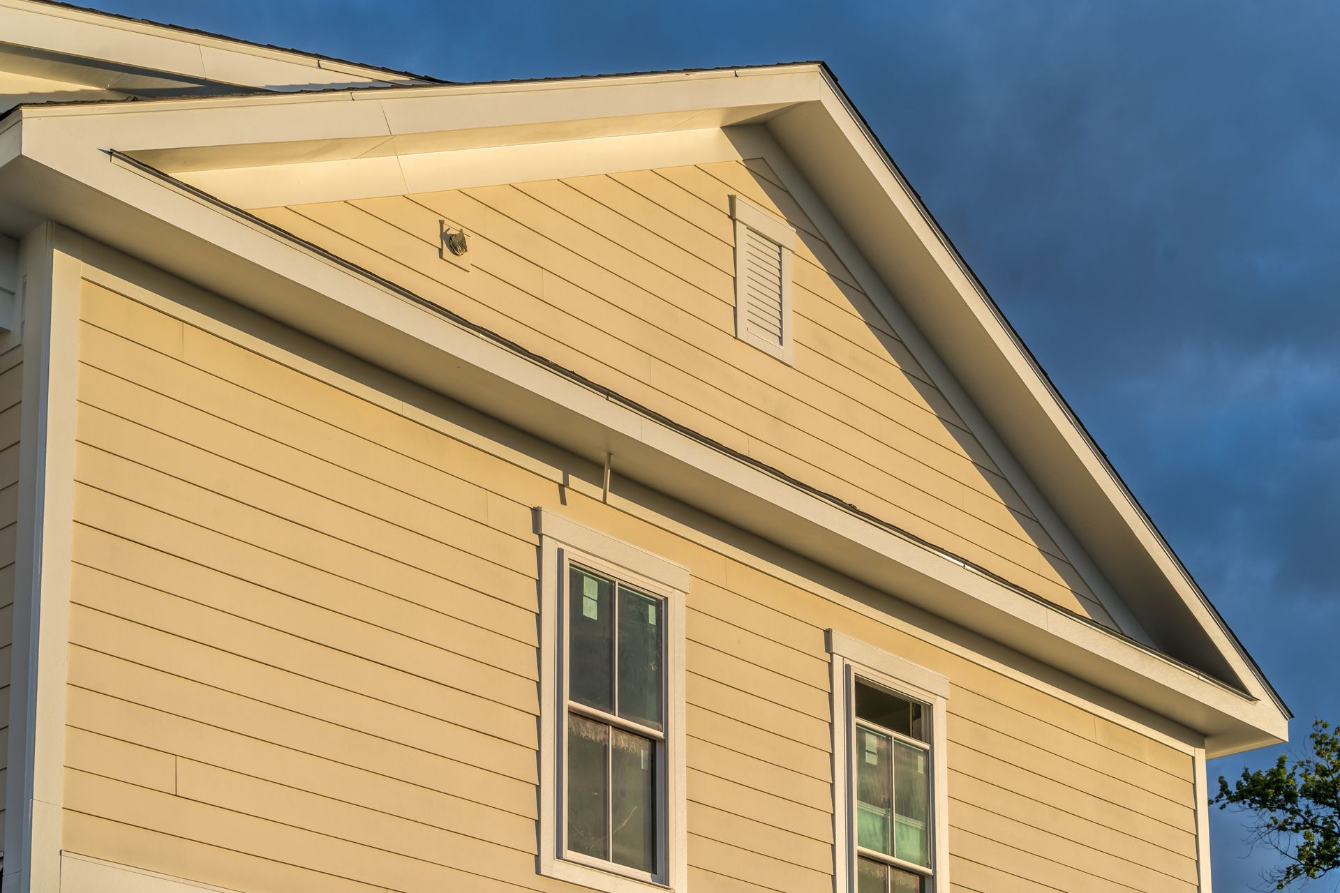 A two-story house with cream-colored horizontal siding, white trim, and a gable roof against a deep blue sky.