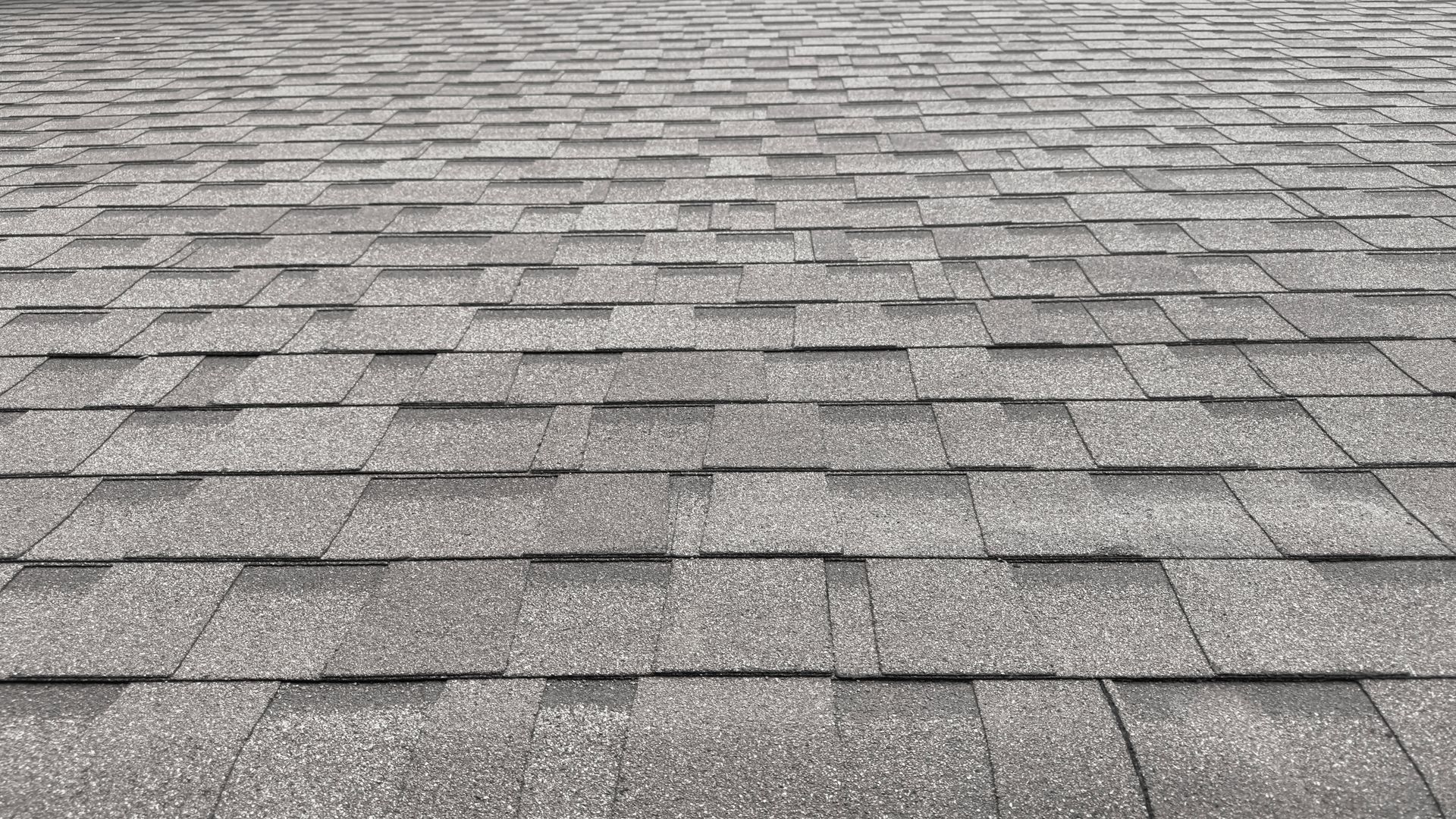 Gray shingled roof seen from above, showing rows of asphalt shingles and a ridge line