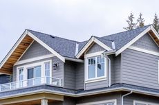 Gray house with white trim and a balcony under a cloudy sky.