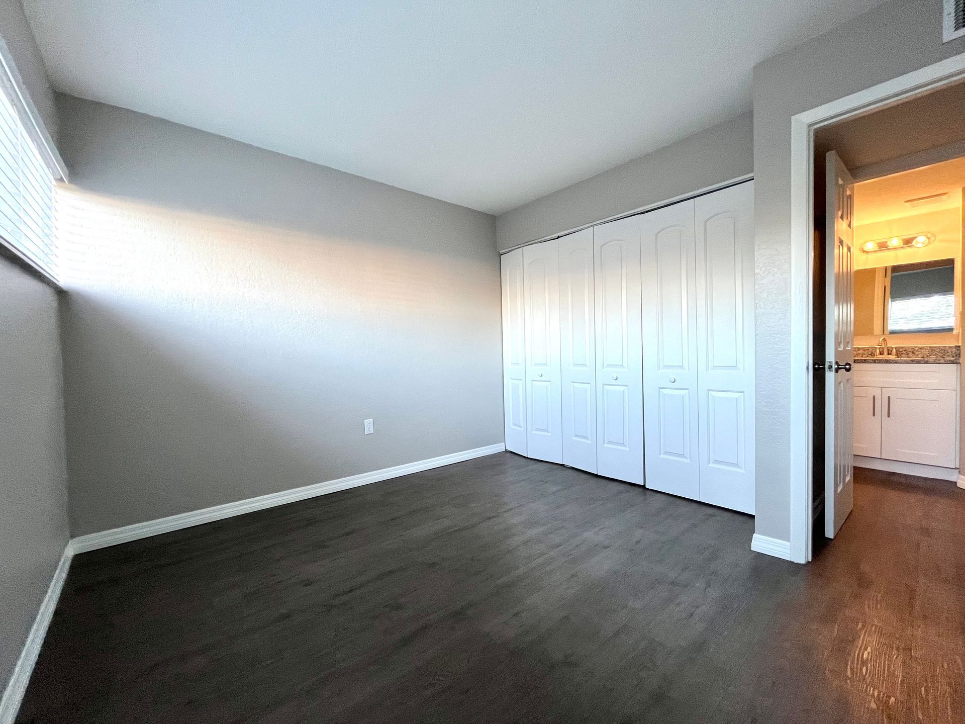 Bedroom with dark wood floor, light gray walls, white closet doors, and bathroom entrance.