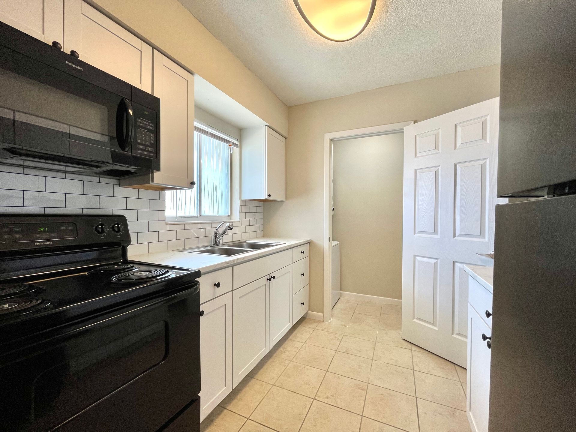 White kitchen with black appliances and white cabinets; light beige floor and walls.