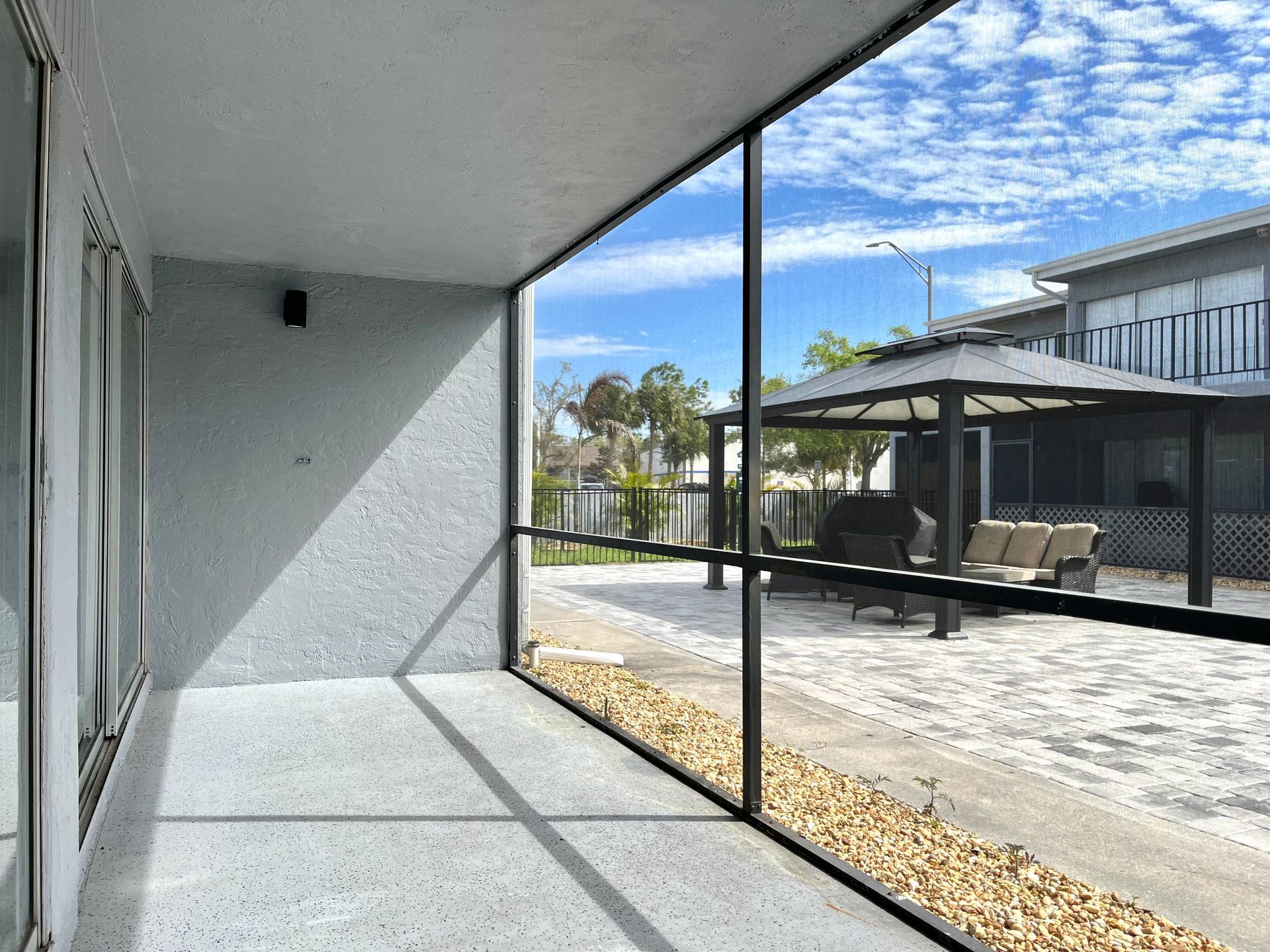 A screened-in porch with a view of a patio, gazebo, and blue sky.
