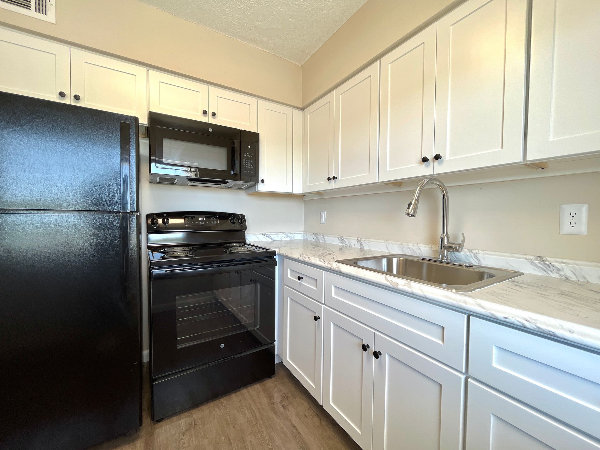 A small kitchen with white cabinets, black appliances, and a marble-patterned countertop.
