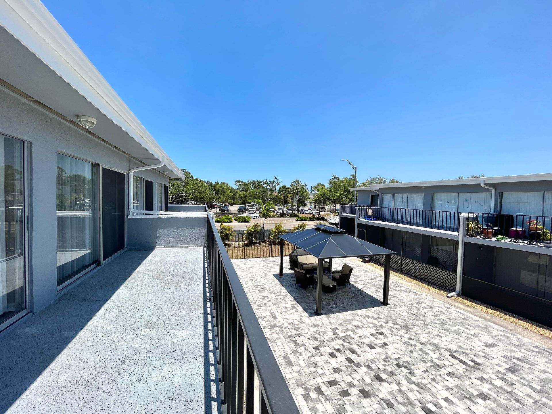 View from a balcony overlooking a patio with a gazebo, a street, and buildings on a bright sunny day.