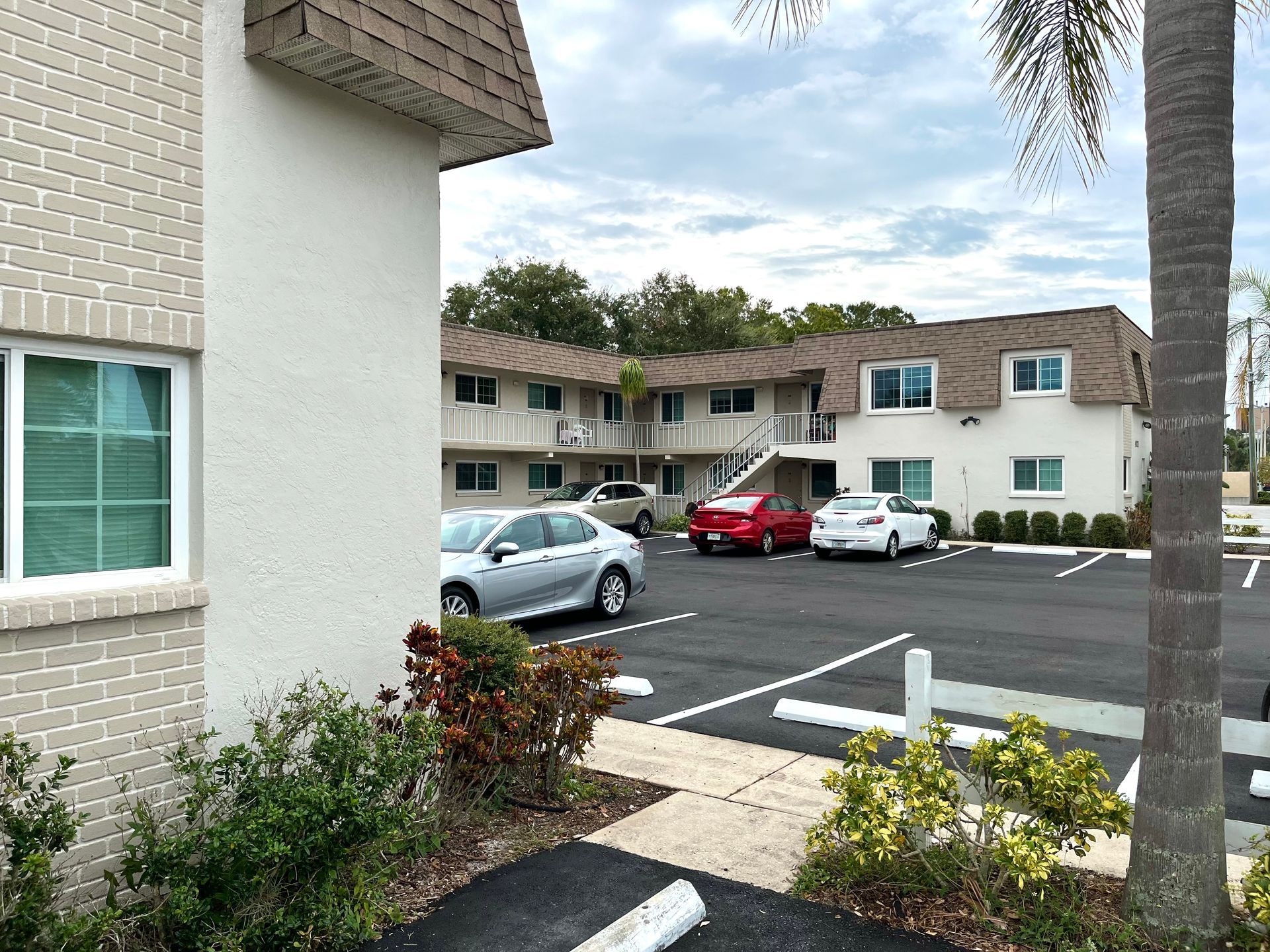 Exterior view of an apartment building with parking lot and cars on a cloudy day.