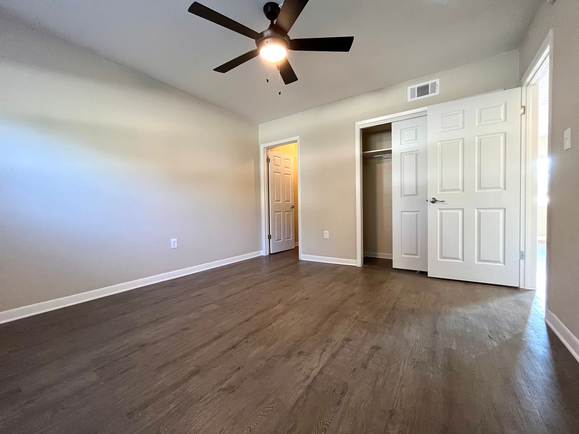 Empty bedroom with dark wood floors, closet, ceiling fan, and two doorways.