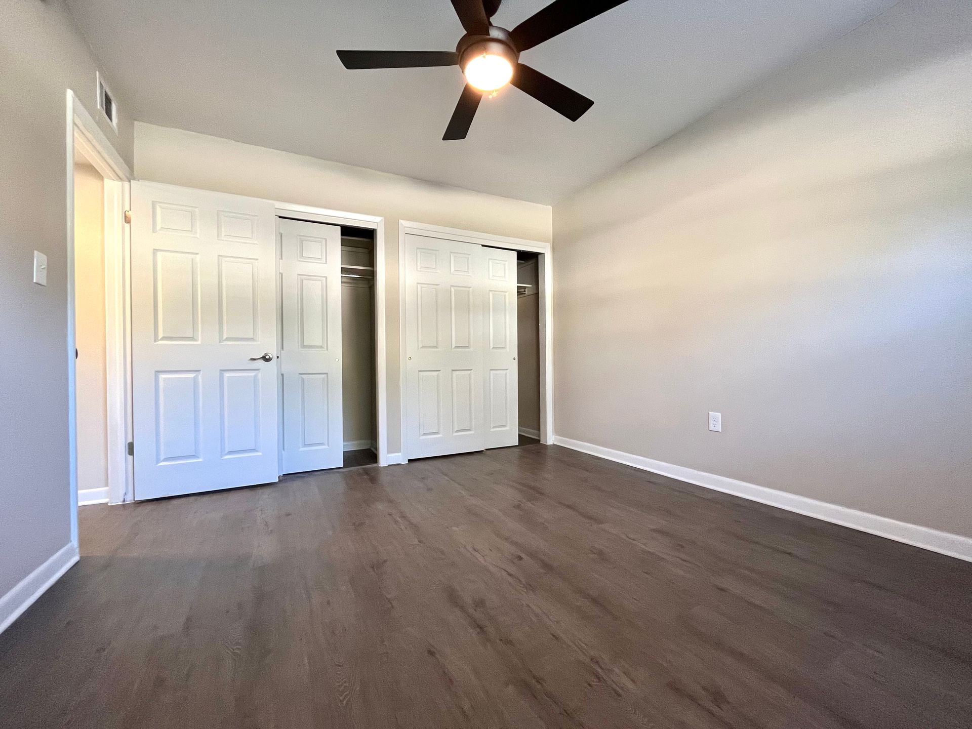Empty bedroom with wood-look floor, white doors and walls, ceiling fan.