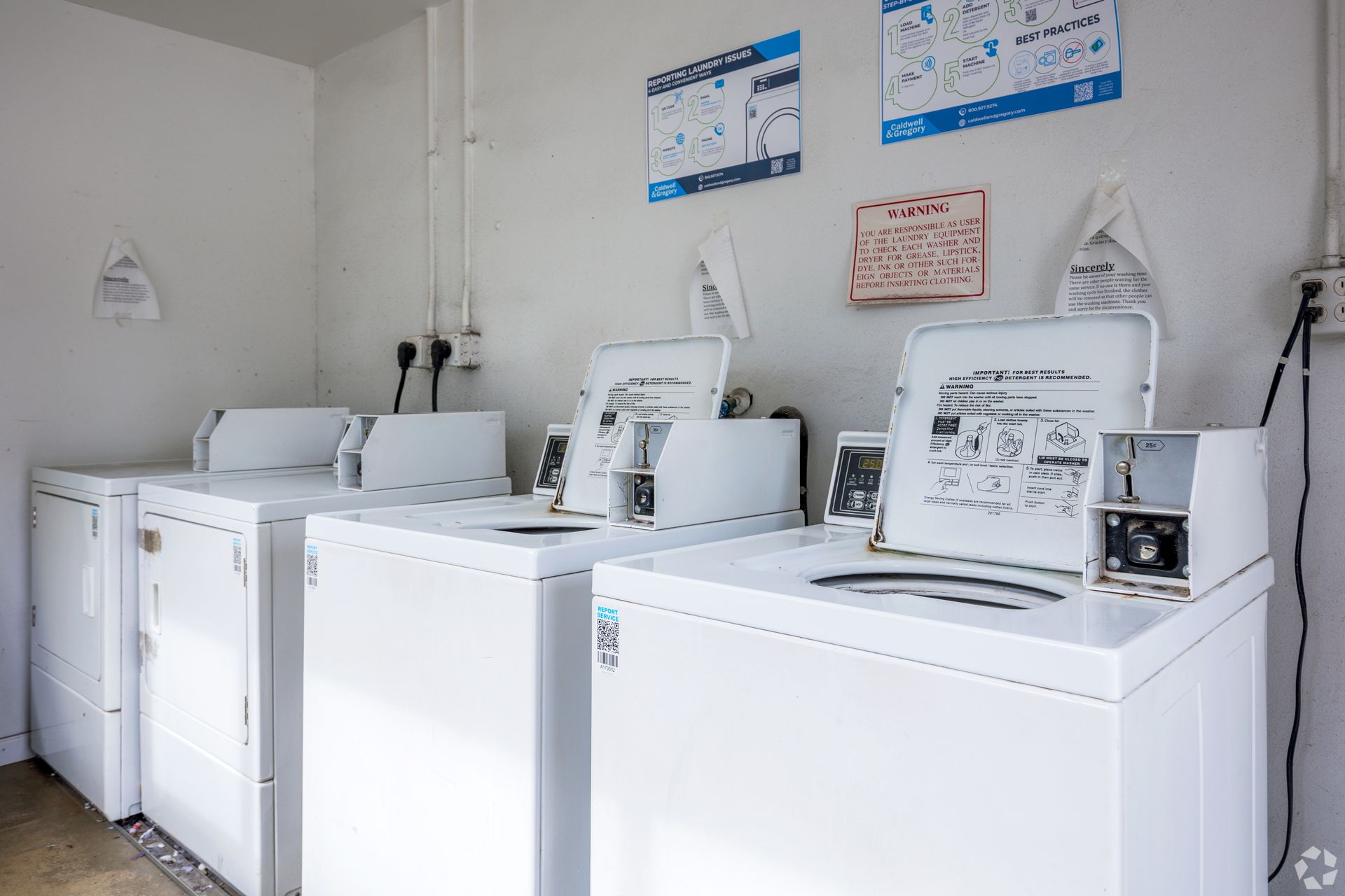 Laundry room with white washers and dryers, instructions on the wall.