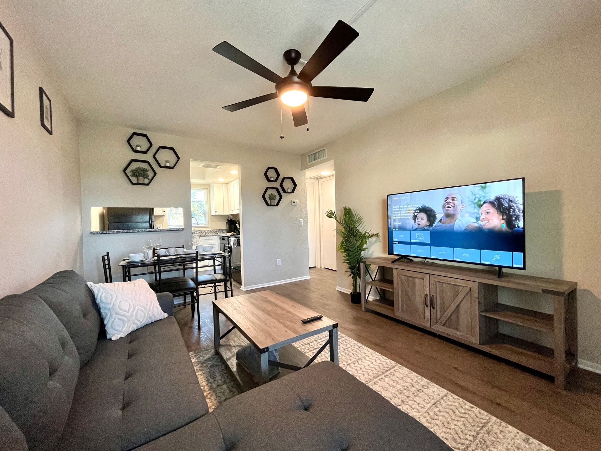 Living room with gray sectional, TV, wood coffee table, open to dining area and kitchen.