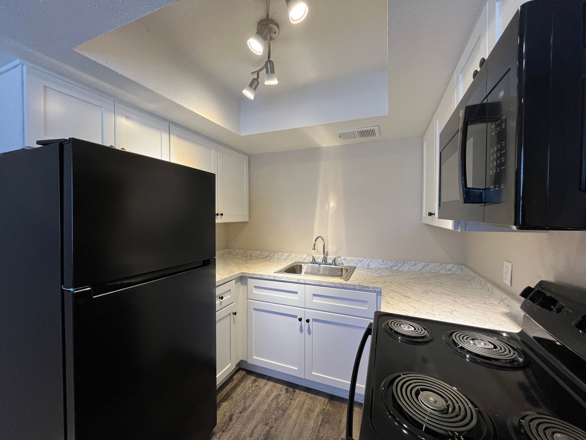 Kitchen with black appliances, white cabinets, light countertops, and track lighting.