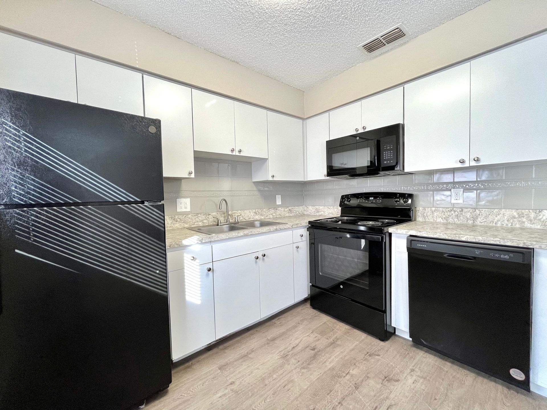 Kitchen with black appliances, white cabinets, and light-colored countertops and flooring.