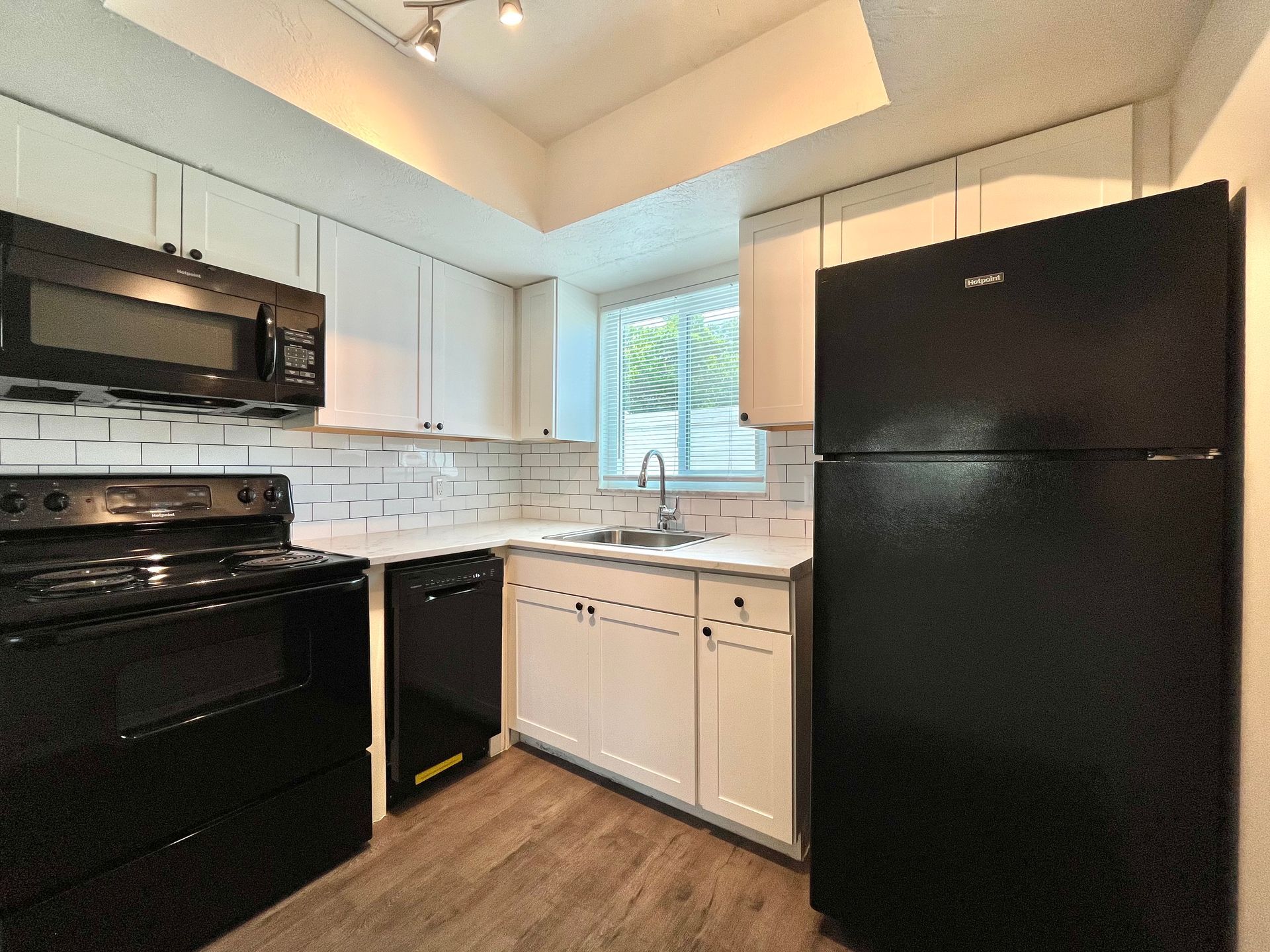 Black and white kitchen with black appliances, white cabinets, and wood-look flooring.