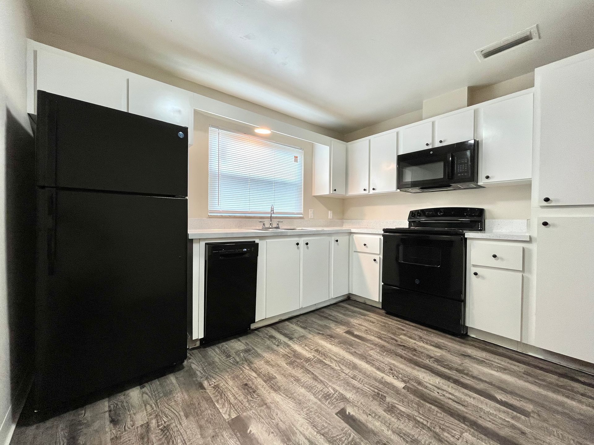 Kitchen with white cabinets, black appliances, and gray wood-look flooring.