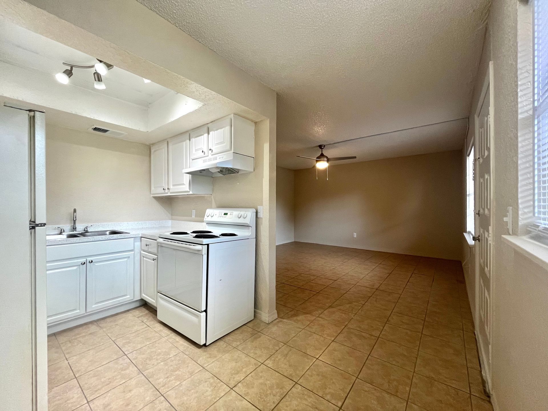 Kitchen with white appliances and cabinets, open to a living area with tiled floors.