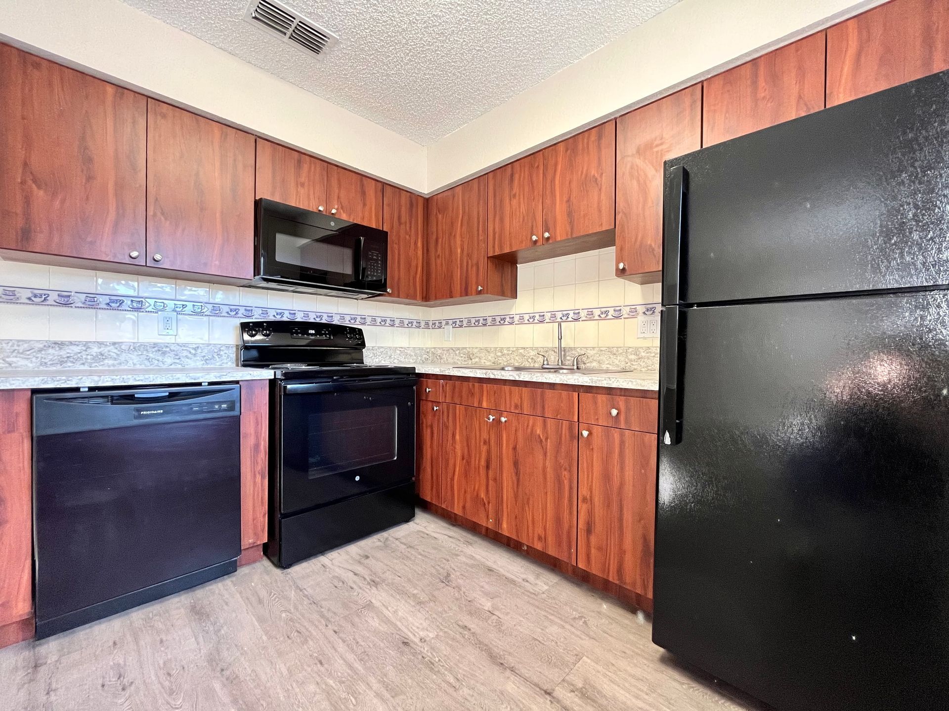 Kitchen with brown cabinets, black appliances, and gray countertops.