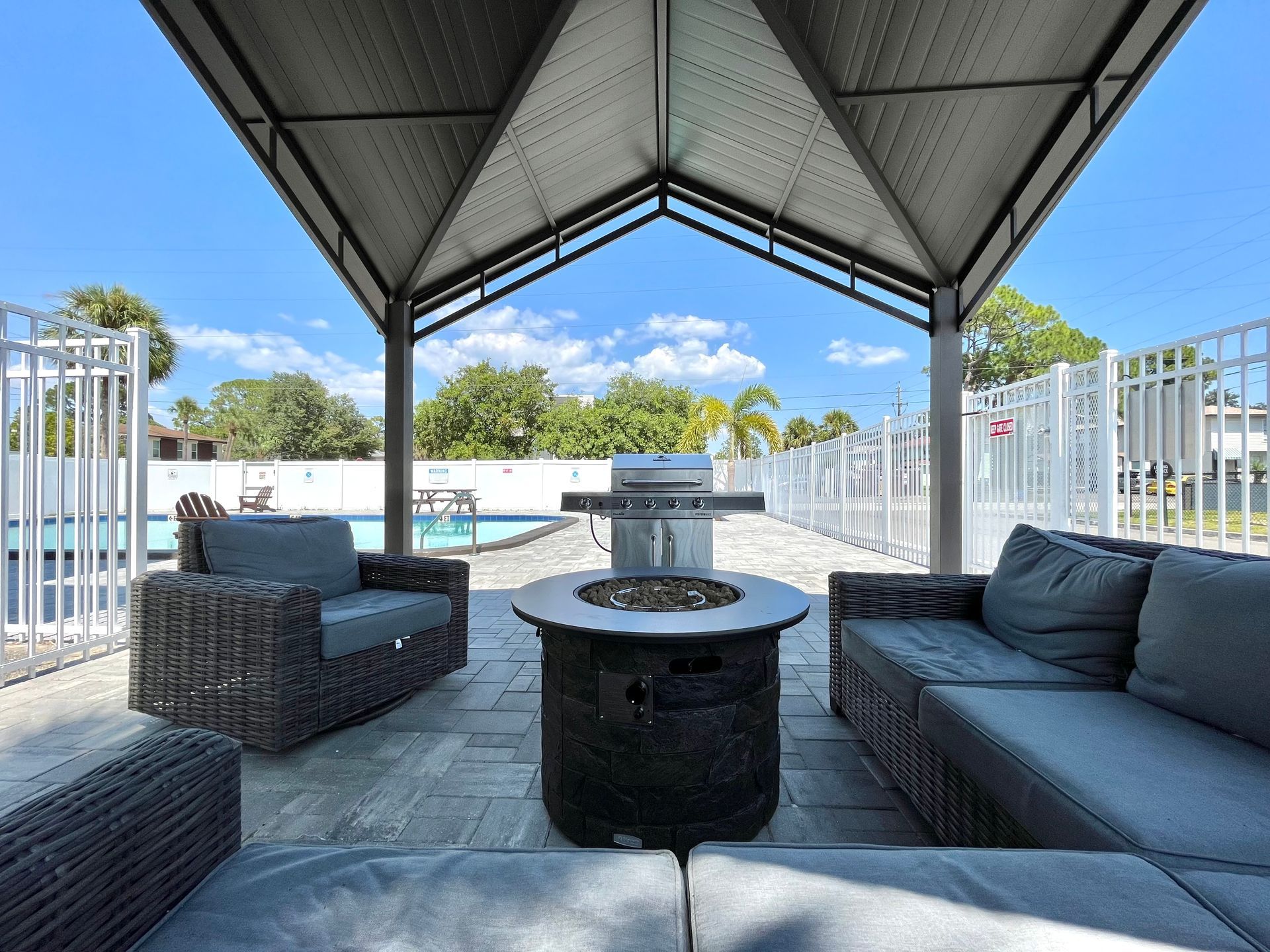 Outdoor seating area with fire pit, grill, and pool view.
