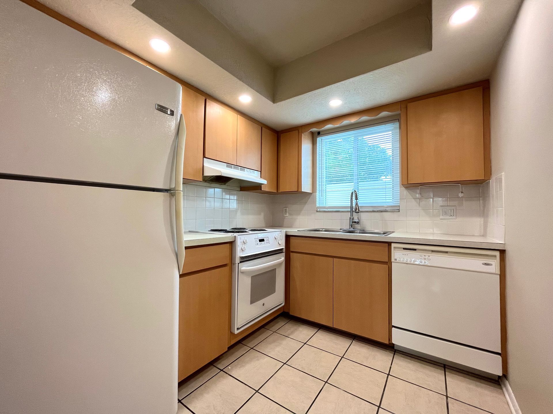 Small kitchen with light wood cabinets, white appliances, and a window.