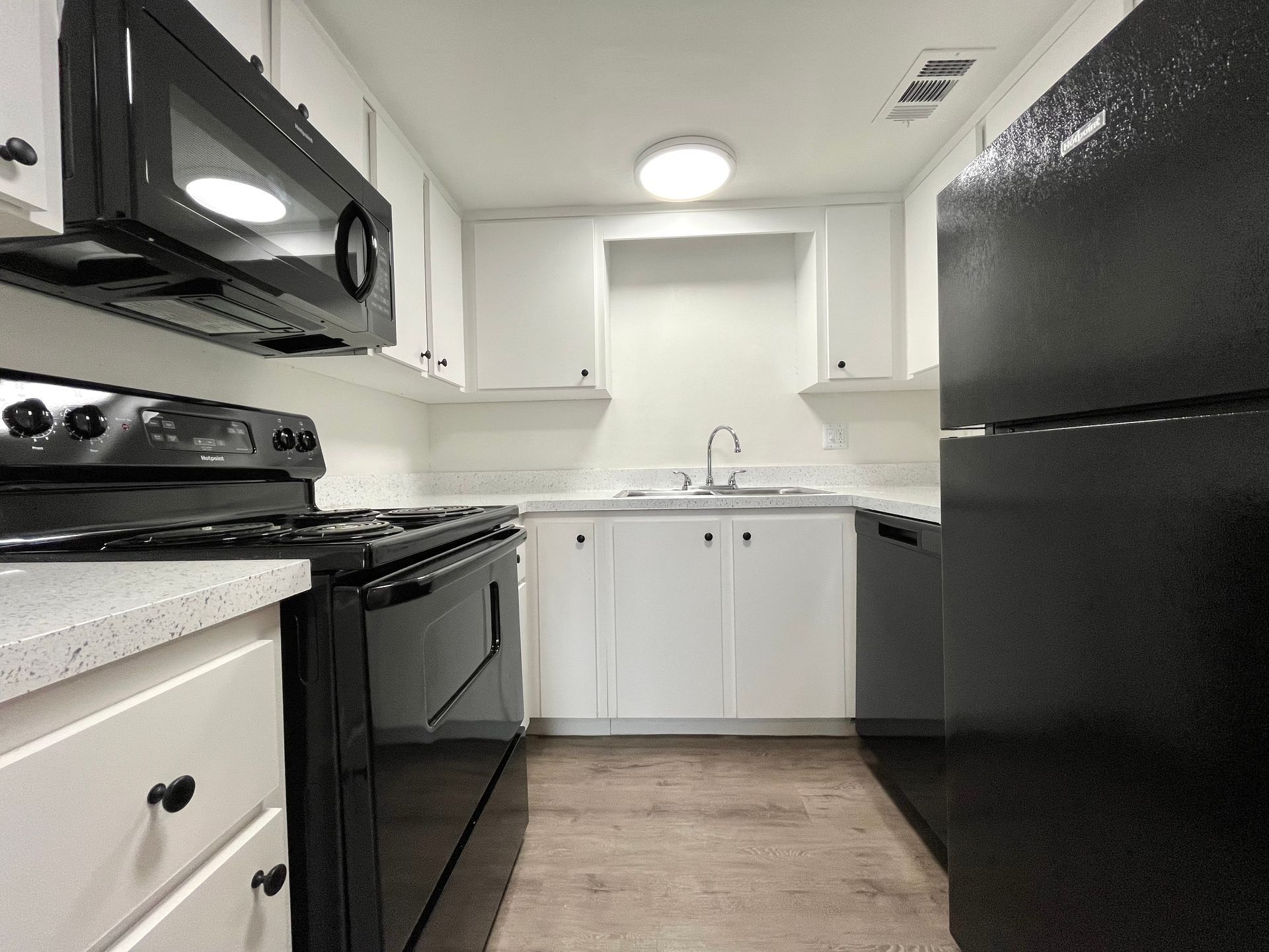 Black and white kitchen with stove, microwave, and refrigerator. White cabinets and countertops.