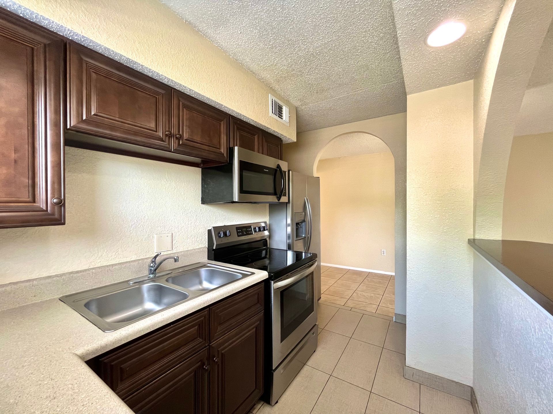Kitchen with dark brown cabinets, stainless steel appliances, and a view into another room.