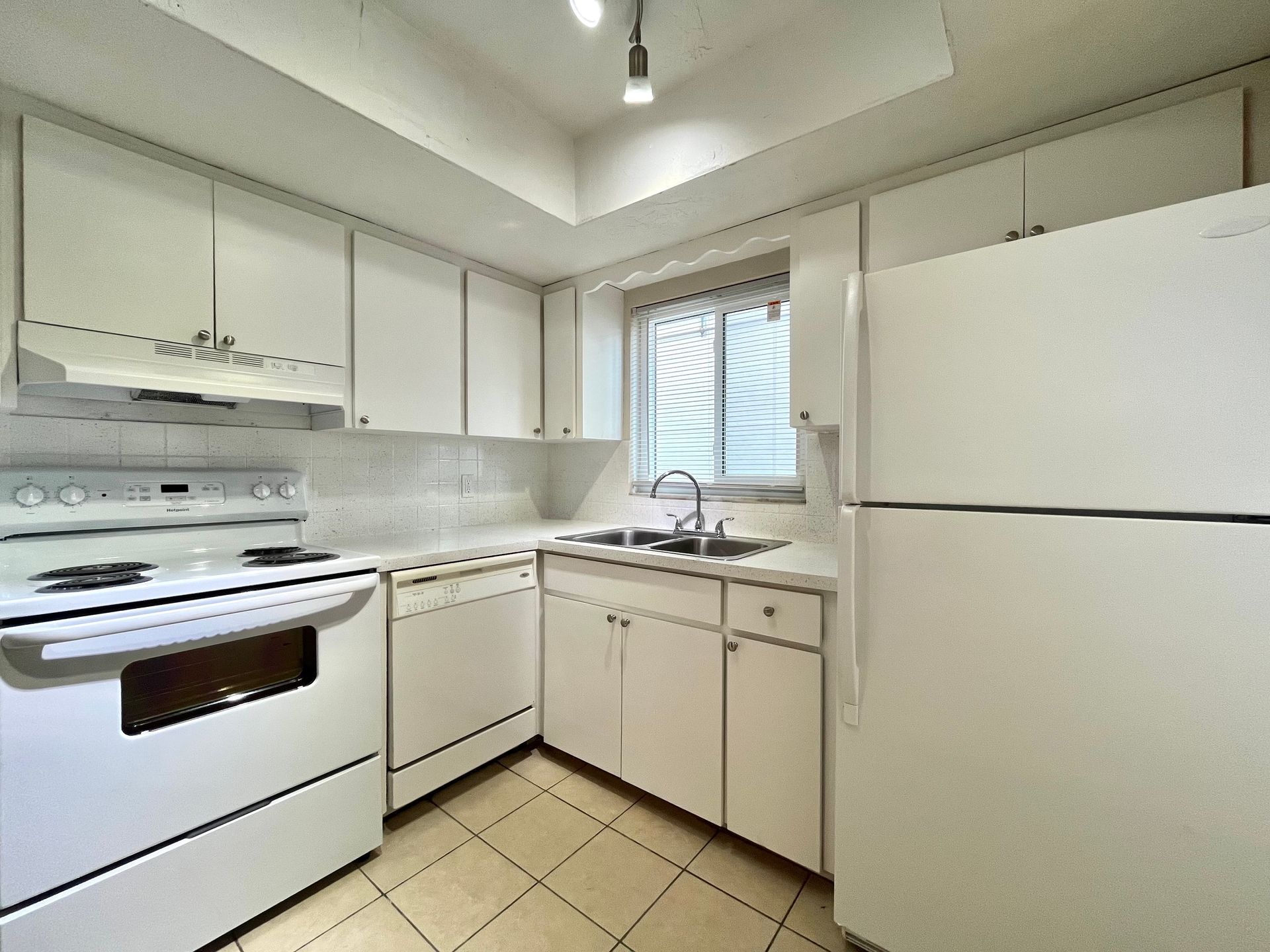 White kitchen with appliances, cabinets, sink, and small window.
