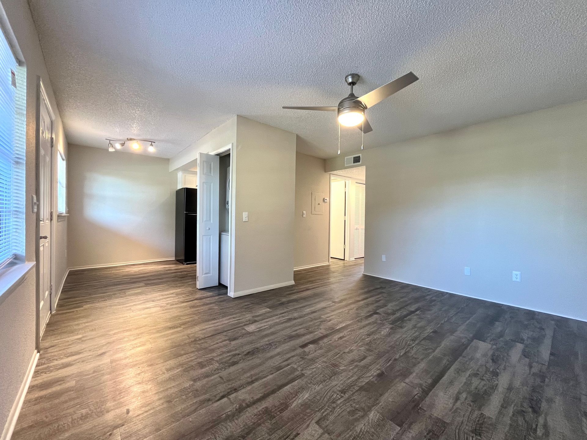 Interior of an apartment: living room with wood floors, ceiling fan, and neutral-colored walls.