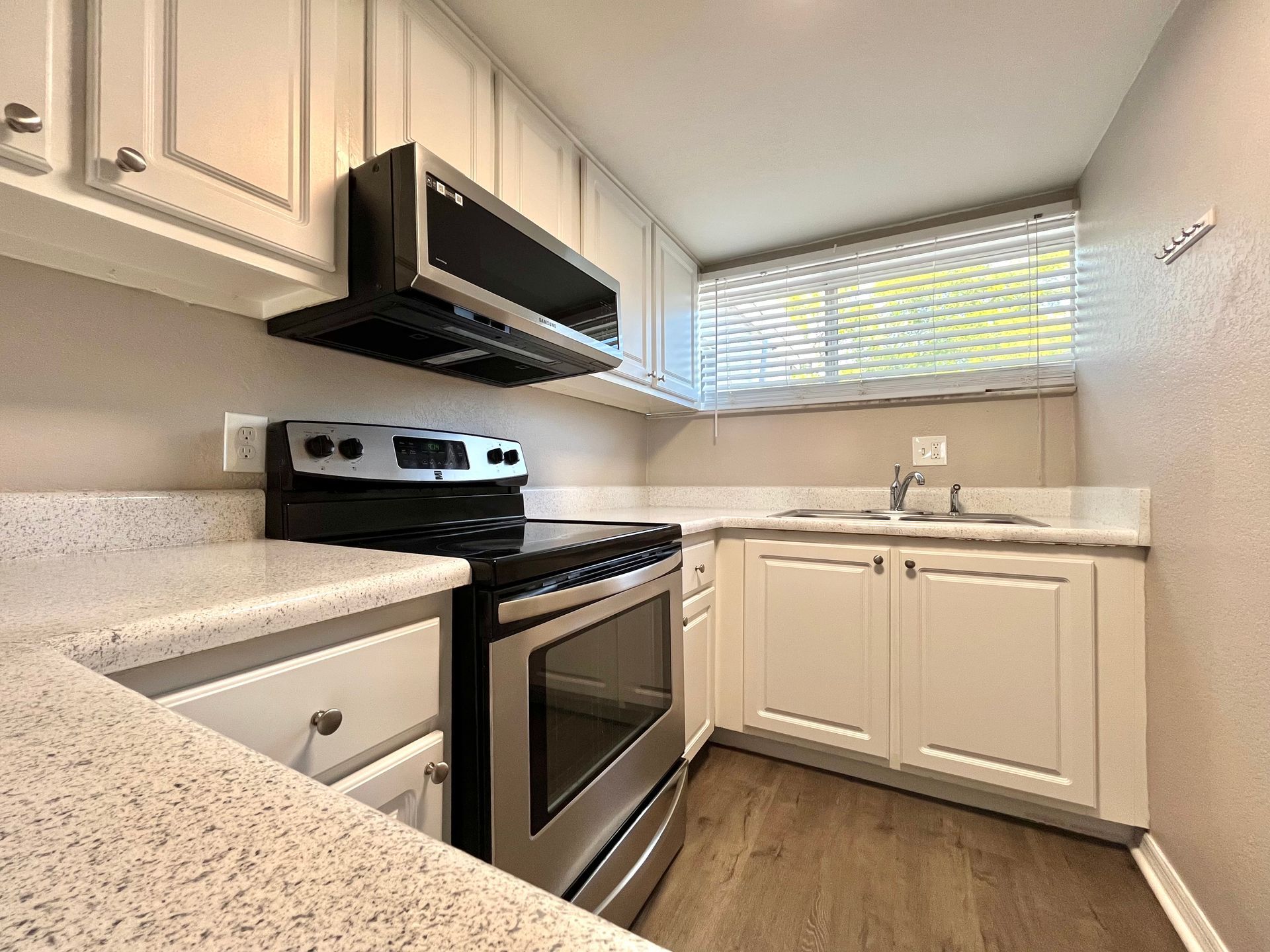 Kitchen with white cabinets, stainless steel appliances, and a window with blinds.