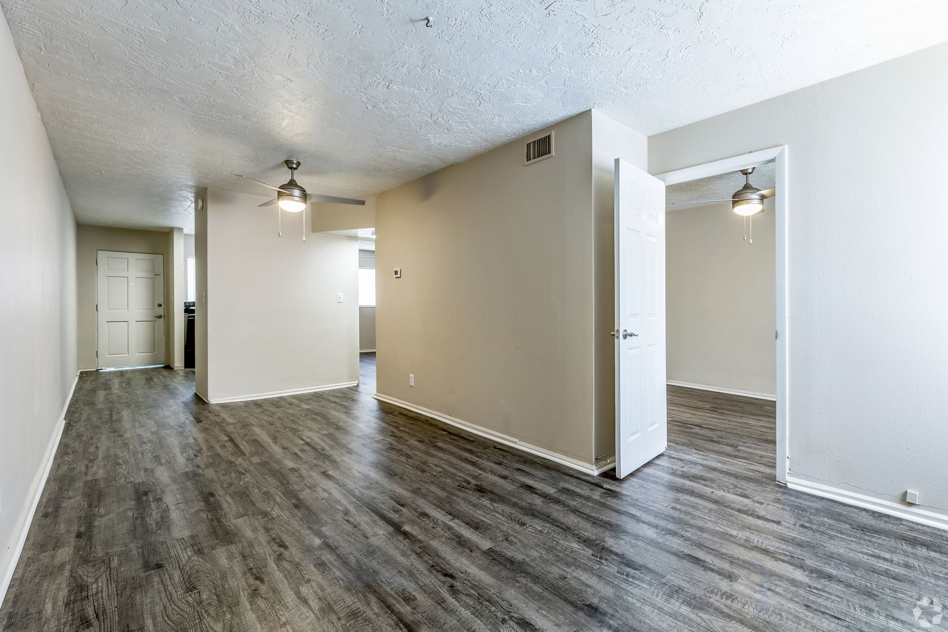 Empty apartment interior with wood-look flooring, beige walls, and ceiling fans.