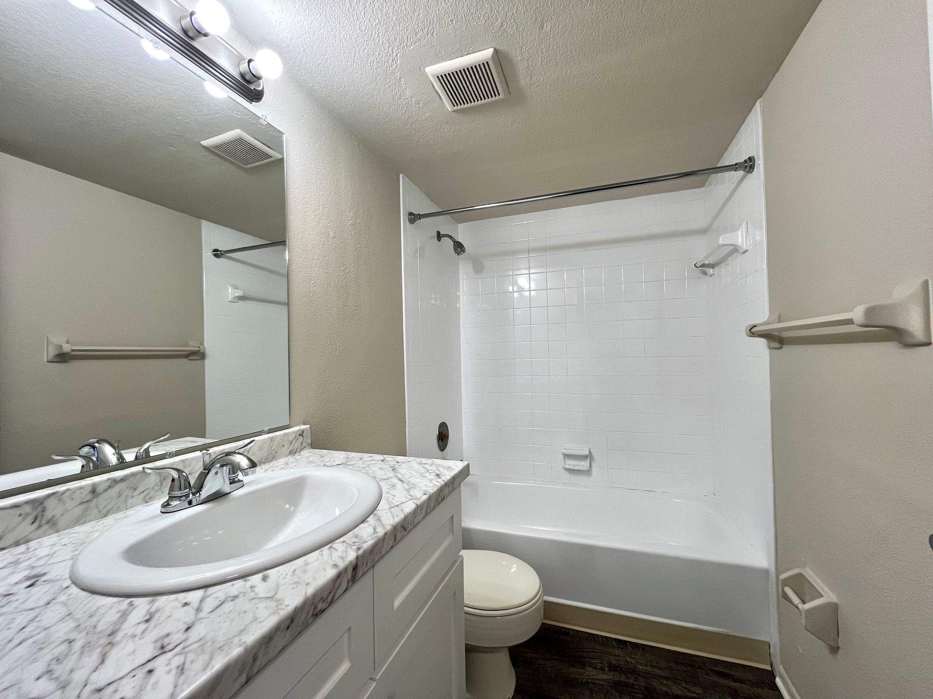 Bathroom with white bathtub, toilet, vanity with marble-look countertop, and mirror.