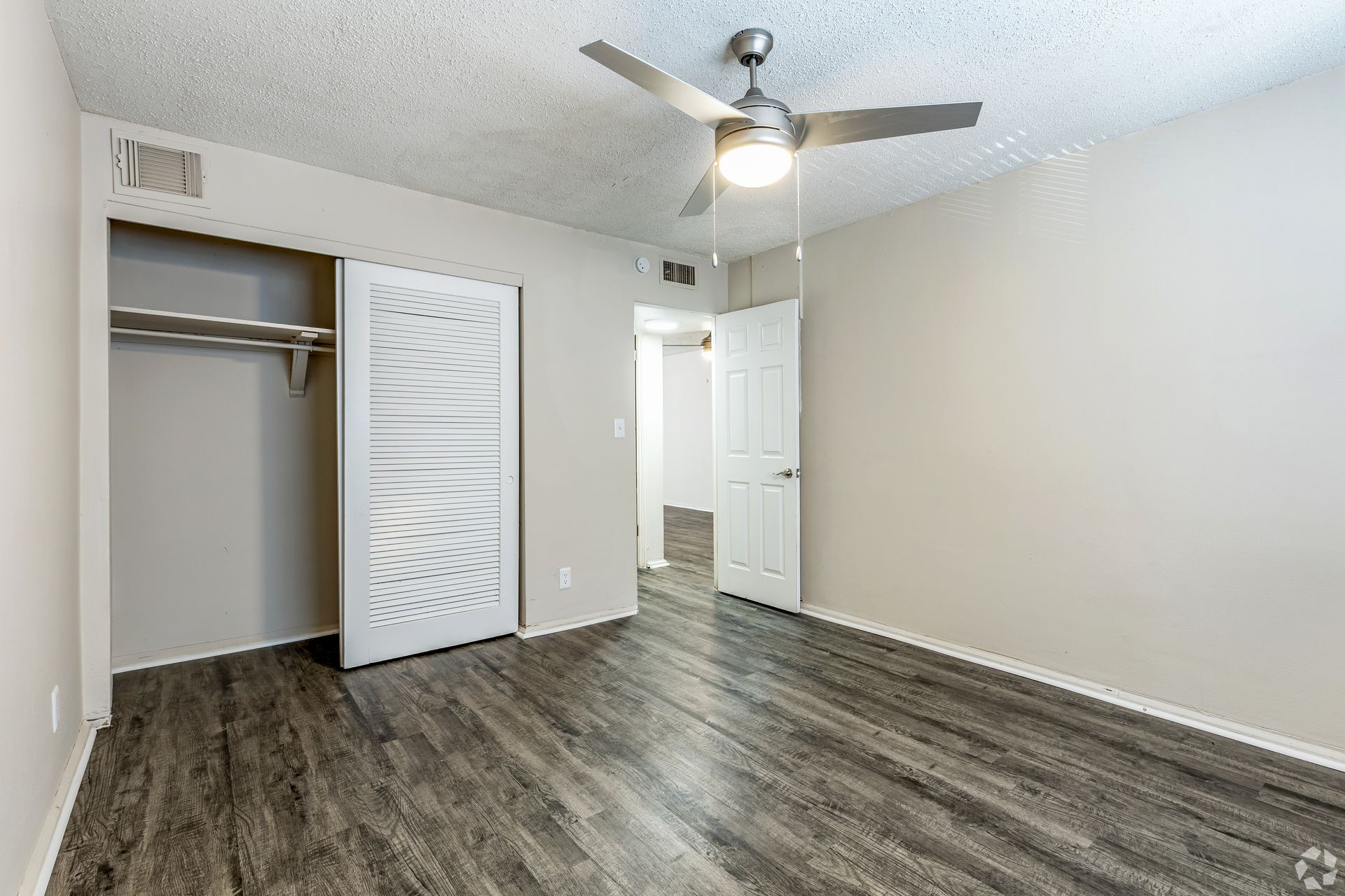 Bedroom with gray wood-look flooring, closet, and a ceiling fan. White walls and door.