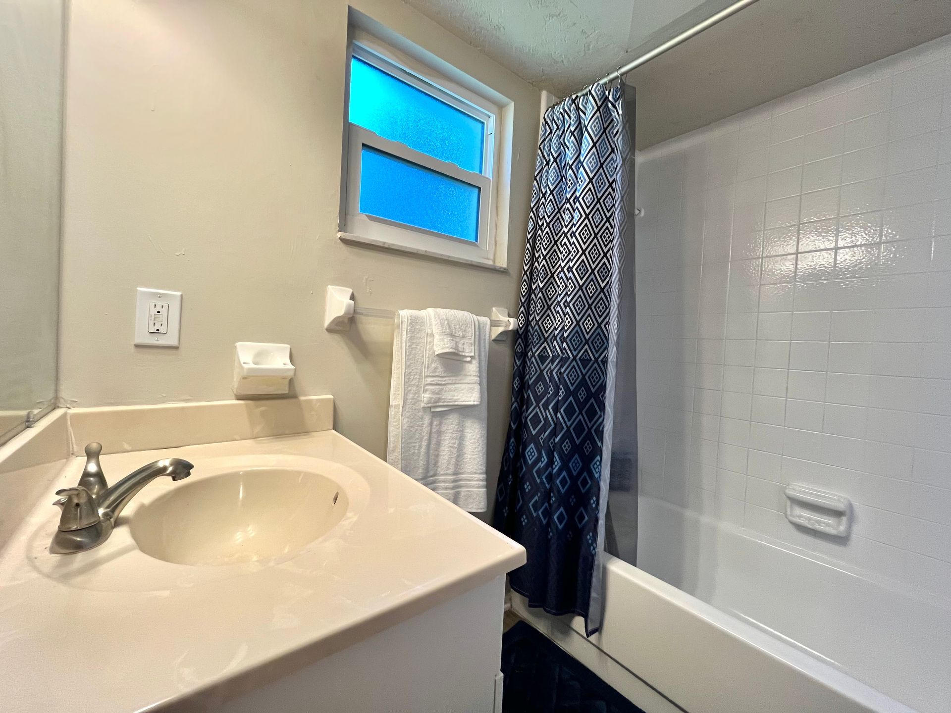 Bathroom with a sink, white tub, blue window, and a shower curtain.