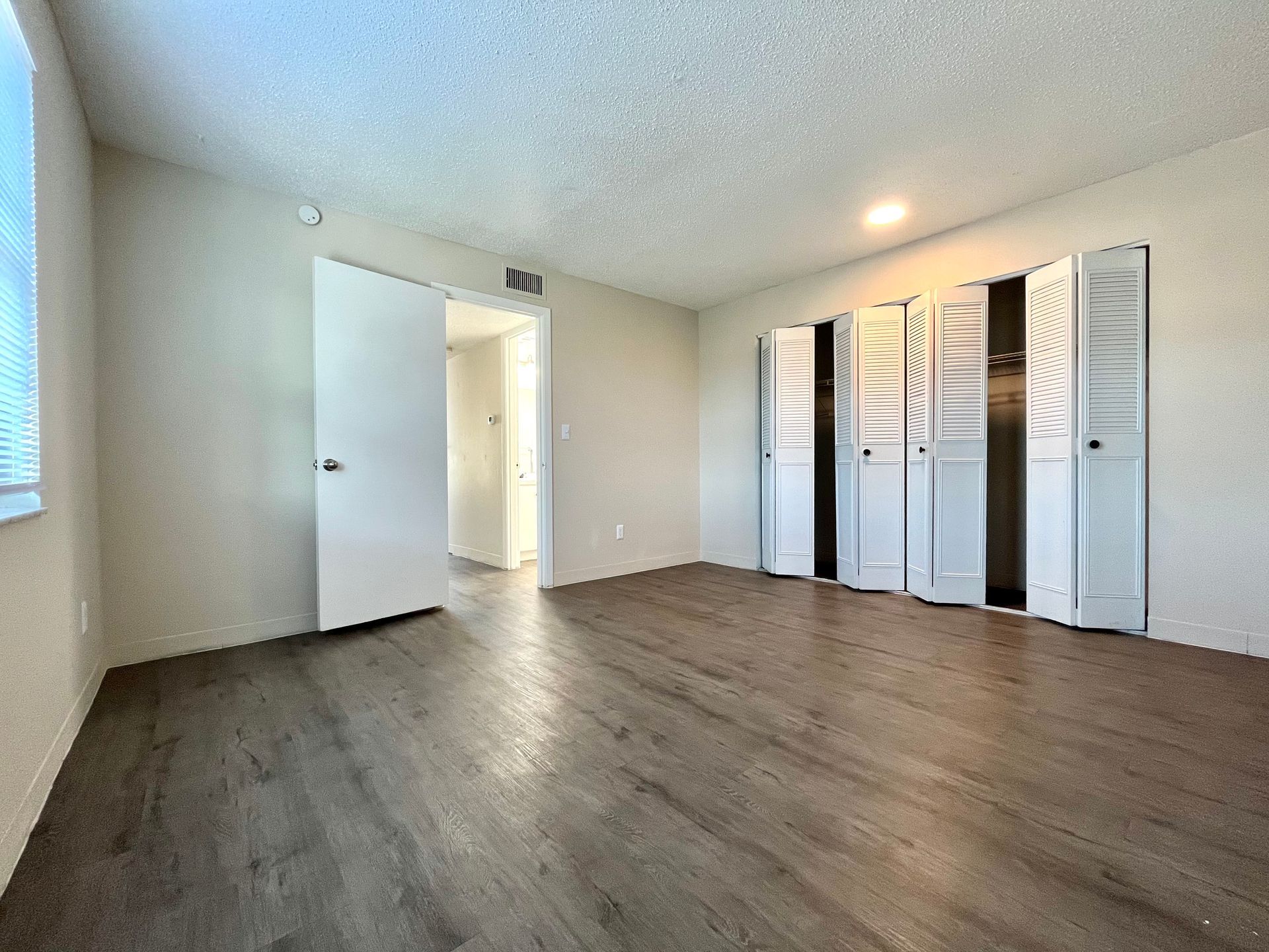 Empty bedroom with light brown wood floors, white bi-fold closet doors, and a doorway to another room.