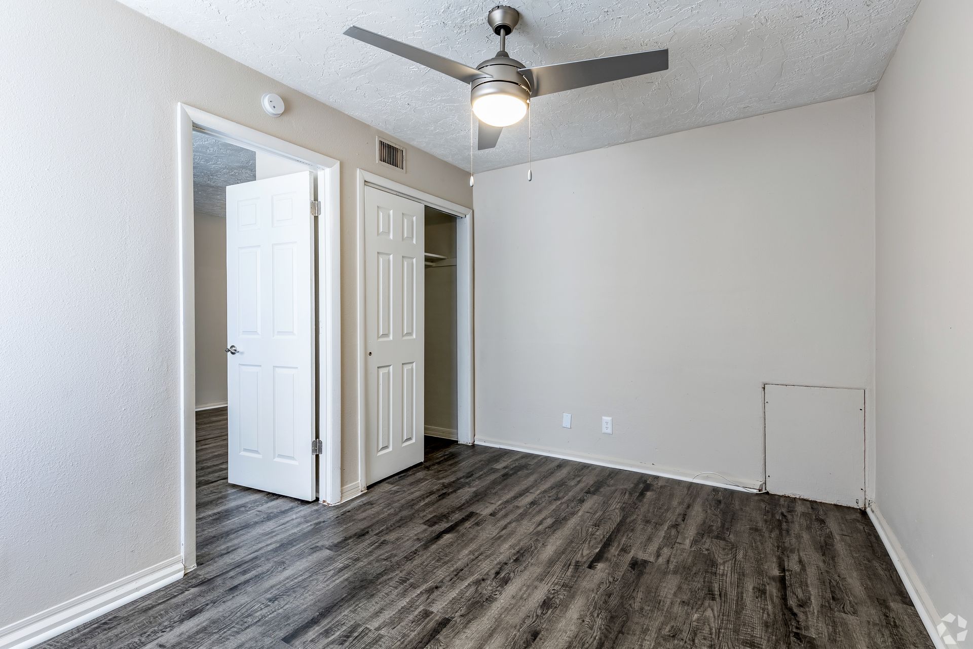 Bedroom with gray wood-look flooring, white walls, ceiling fan, and open doors.