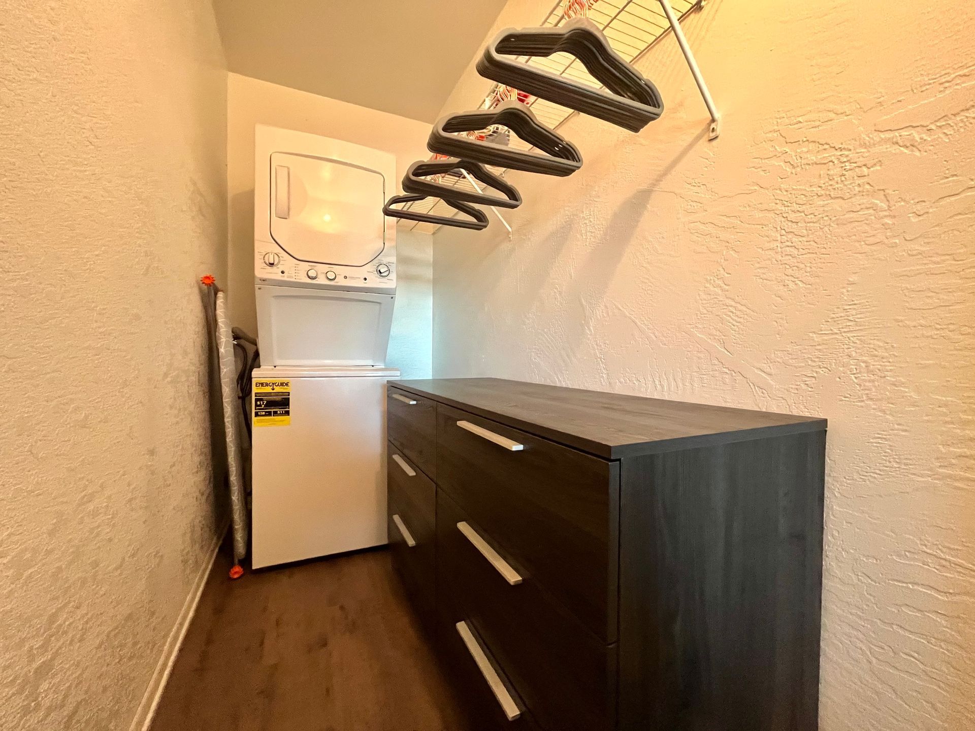 Laundry room with stacked white washer/dryer, dresser, and hanging clothes rack.