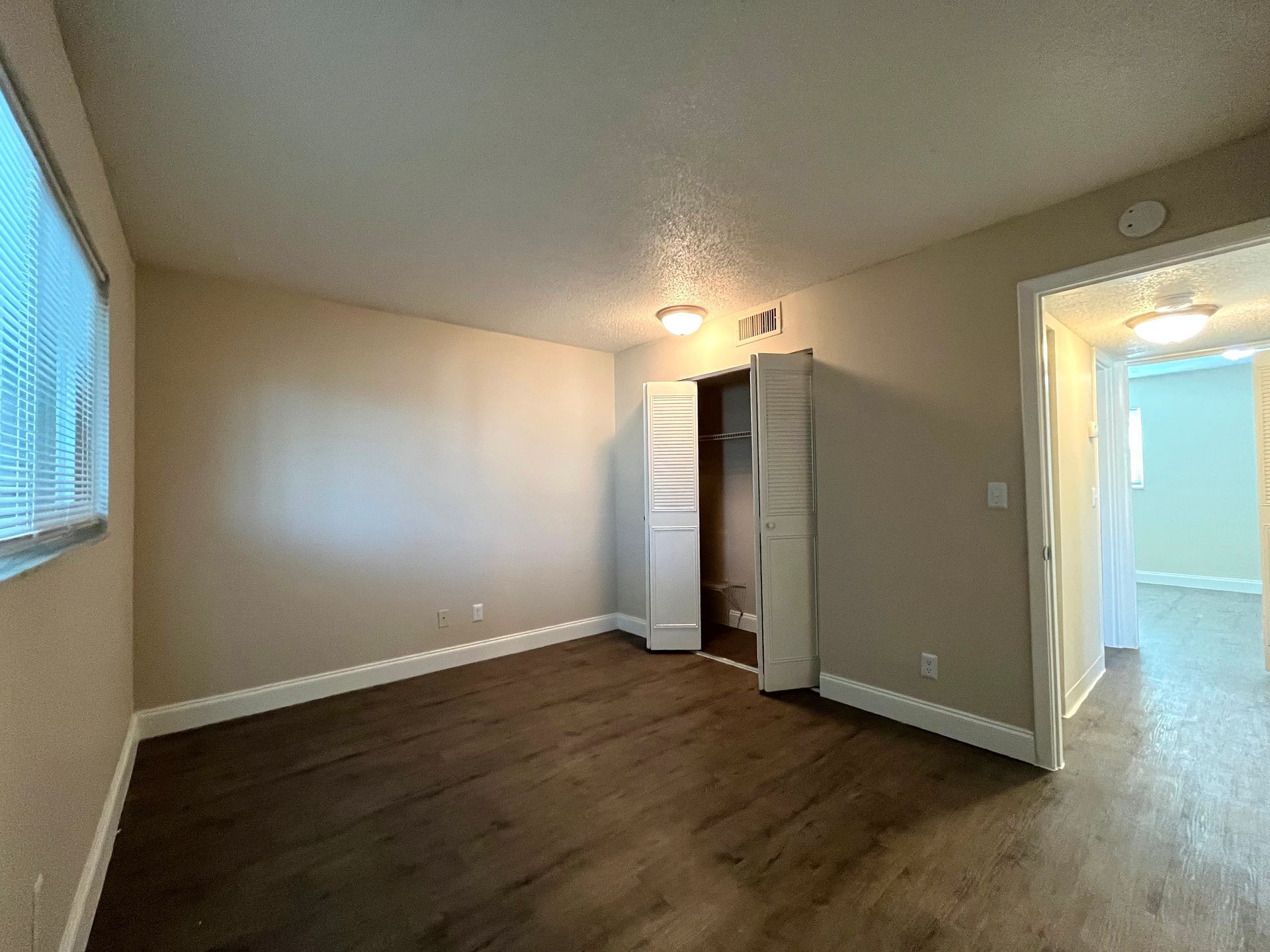 Empty bedroom with wood flooring, closet, and a doorway to another room.