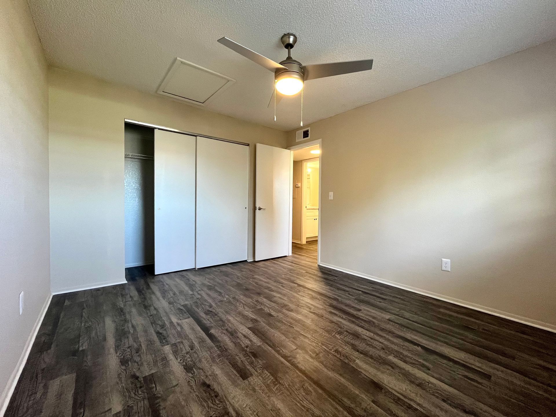Empty bedroom with wood-look flooring, sliding closet doors, and a ceiling fan. Light beige walls.