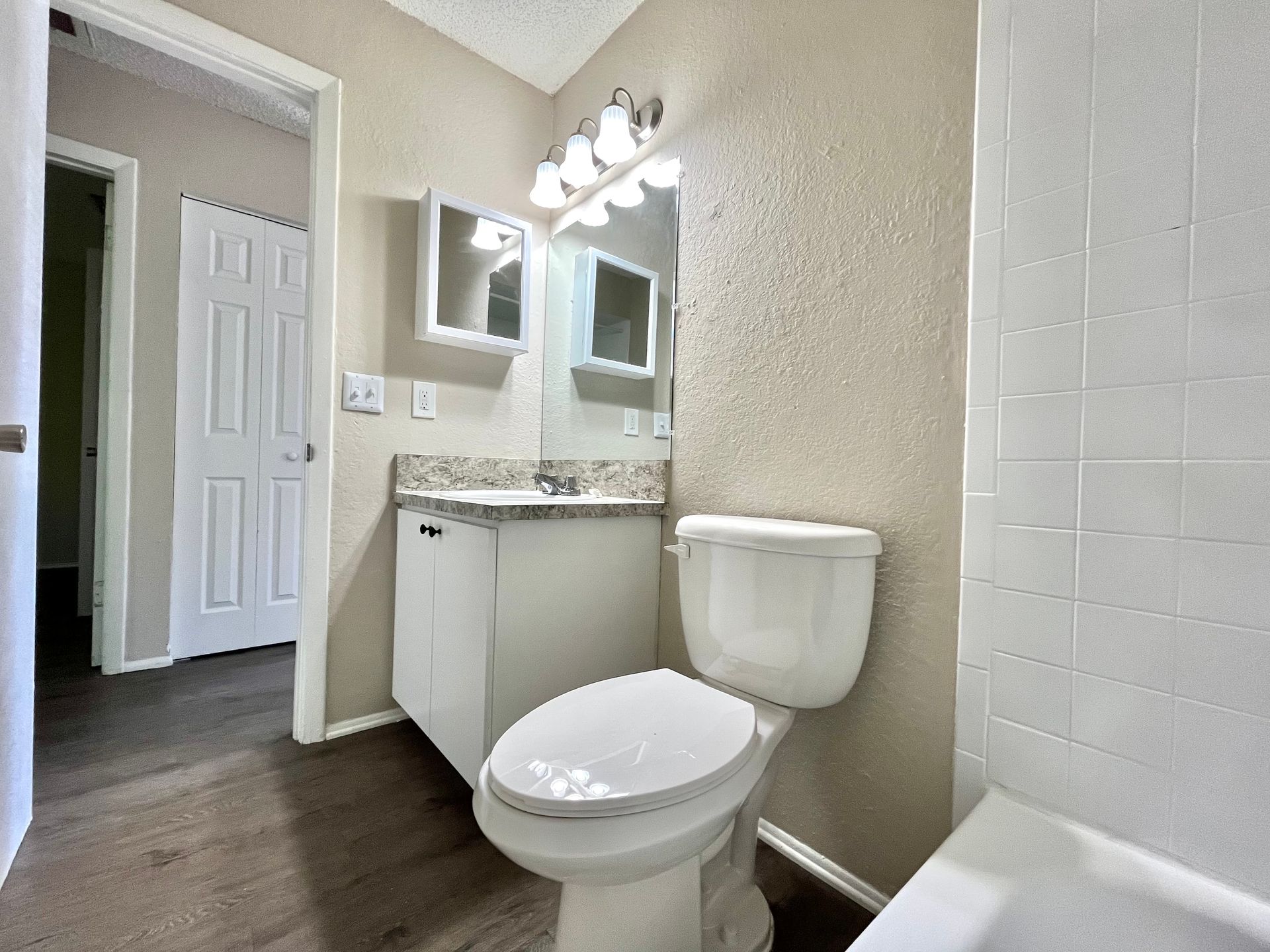 Bathroom with a toilet, vanity, mirror, and doorway. Dark flooring, light walls.
