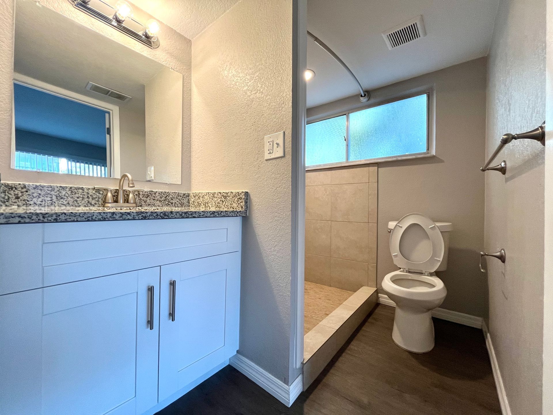 Bathroom with white vanity, gray countertop, toilet, shower, and window.