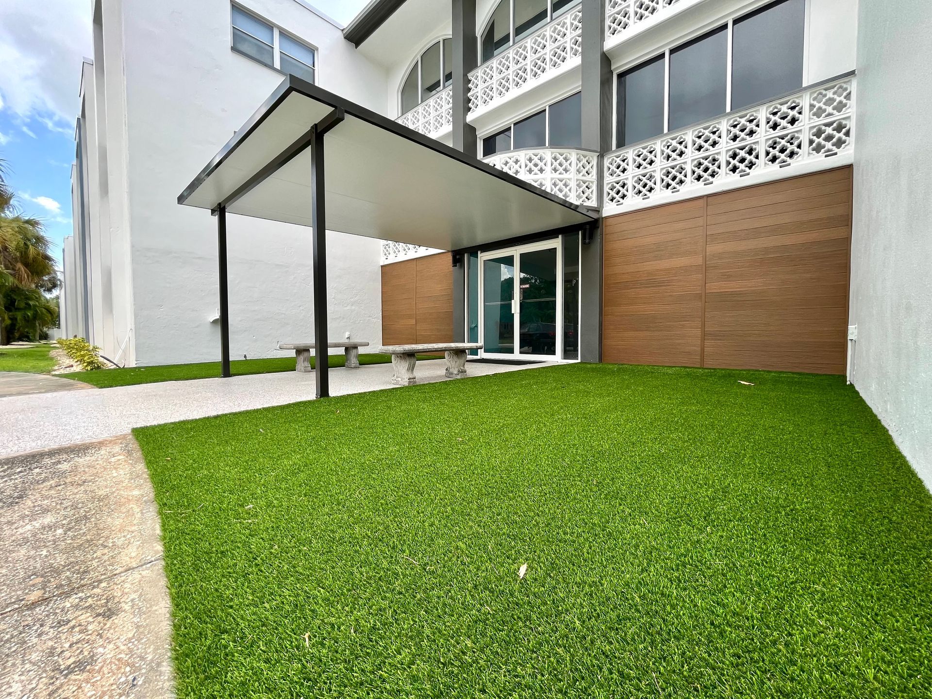Exterior of building with green turf, awning, and benches.