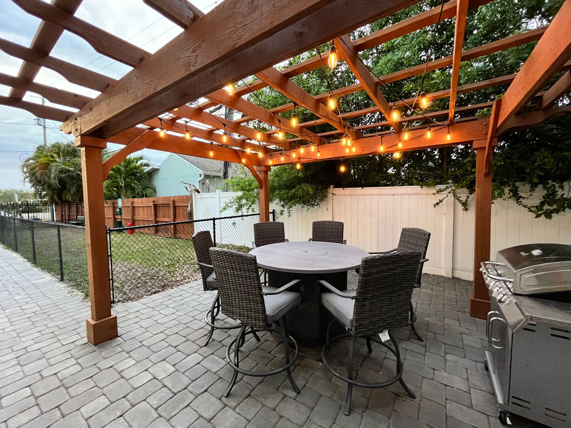 Patio with round table, chairs, pergola with string lights, and a grill.