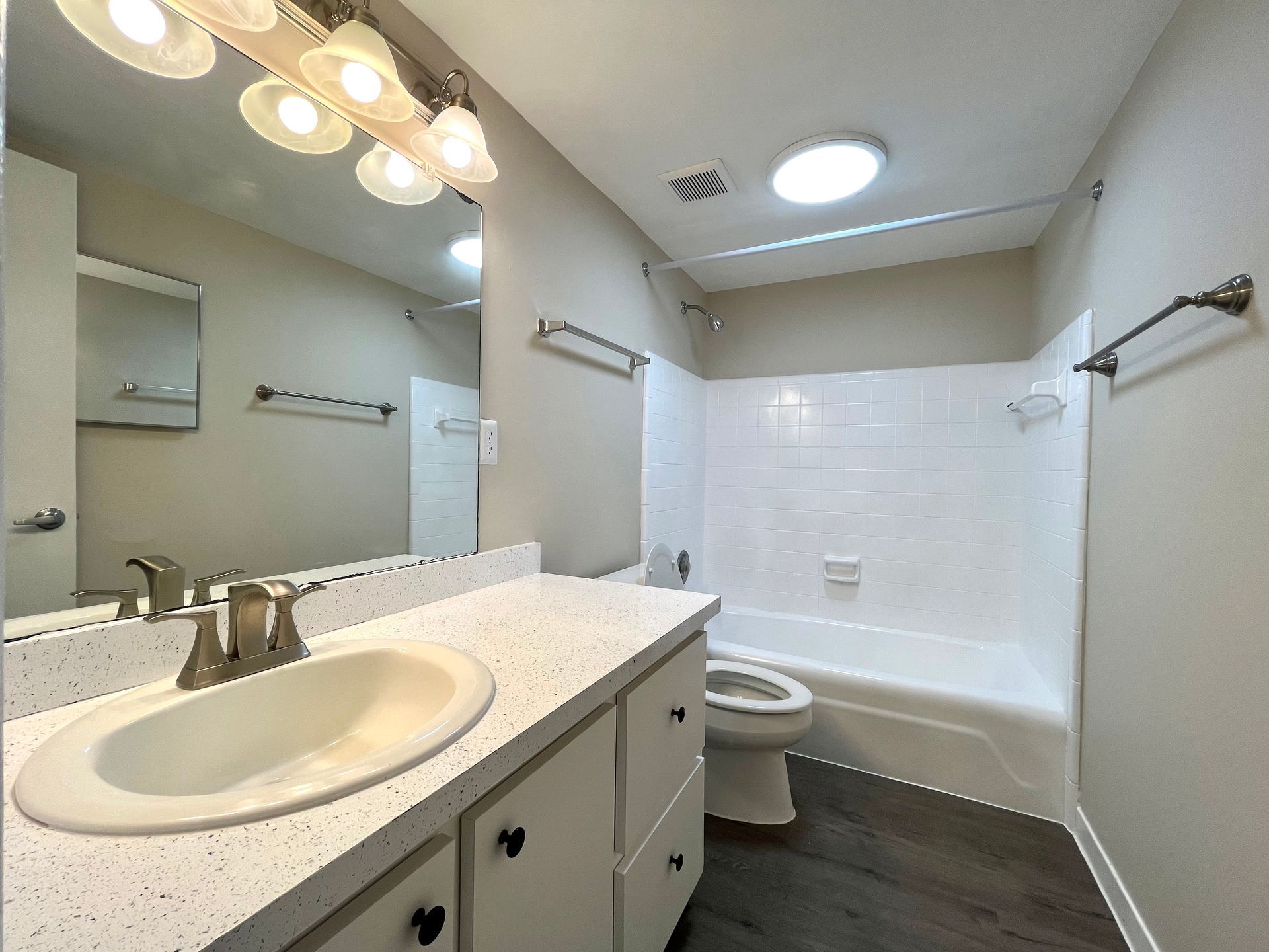 Bathroom with white vanity, toilet, and bathtub, dark wood floor, and light-colored walls.