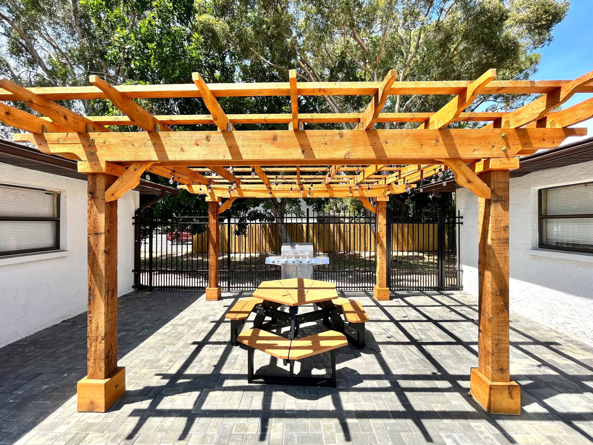 Wooden pergola over a picnic table, casting shadows on a brick patio.