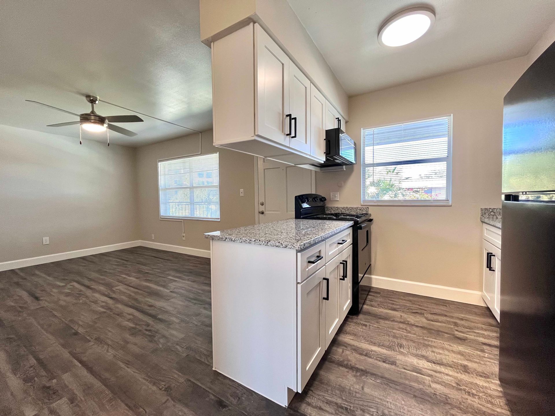 A kitchen with white cabinets, island, stove, and a dark-colored floor.