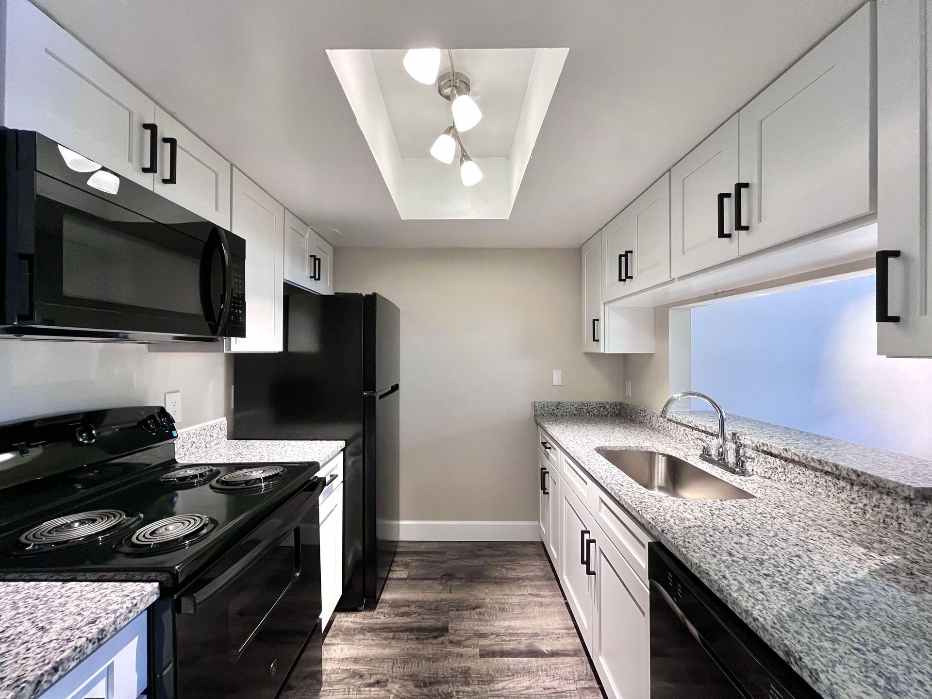 Modern galley kitchen with white cabinets, black appliances, and granite countertops.