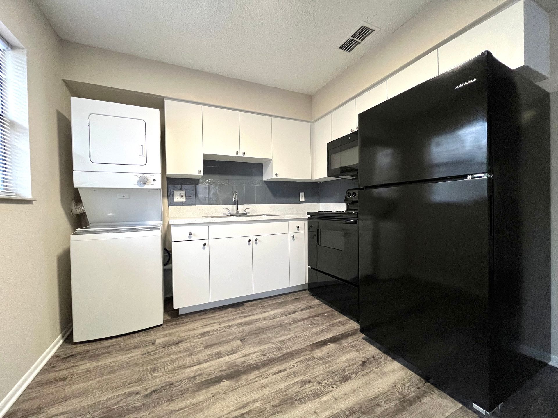 Small kitchen with white cabinets, black appliances, and stacked washer/dryer.